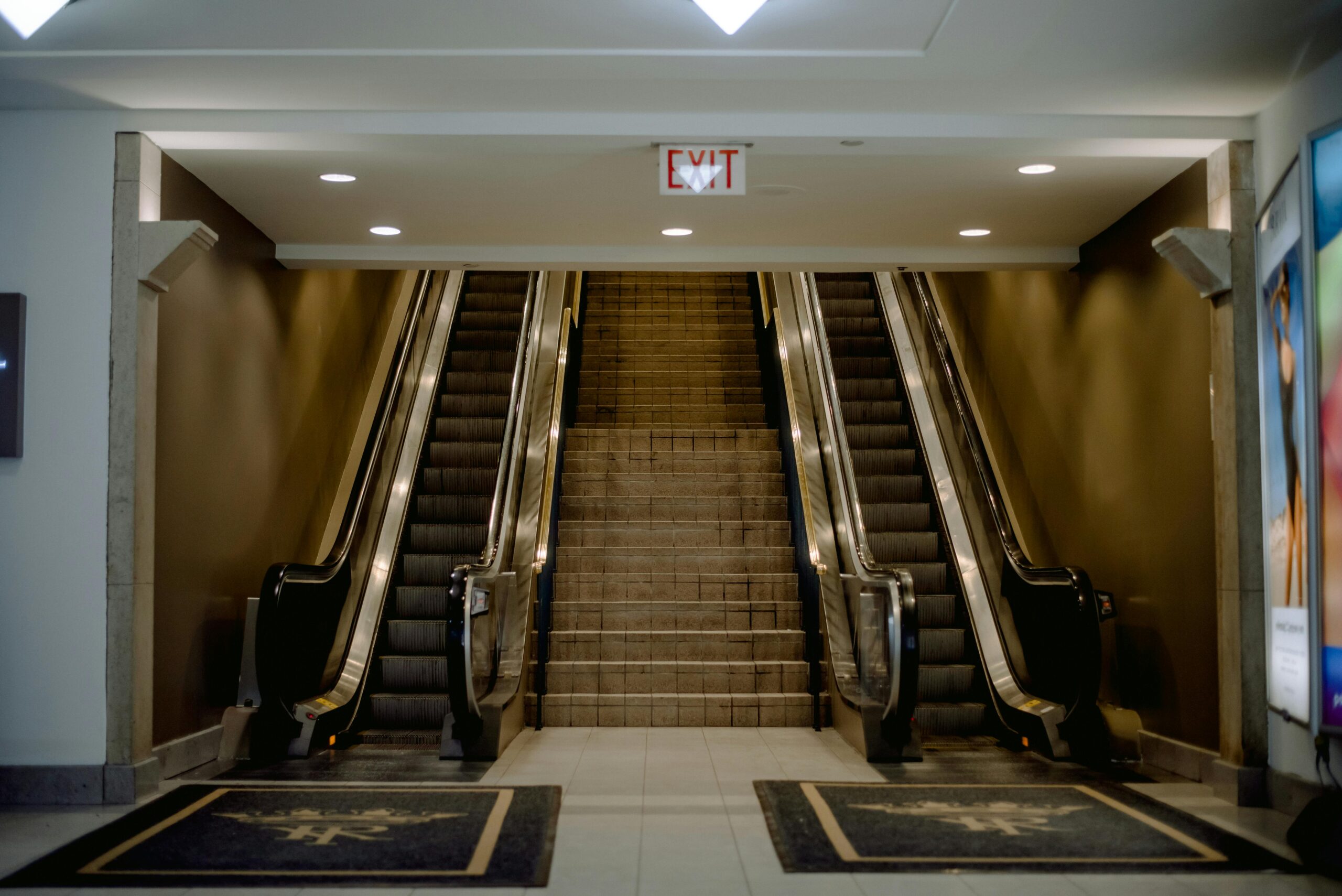 A symmetrical view of escalators and stairs in a well-lit indoor space with exit sign.